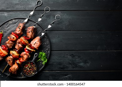 Shish kebab BBQ meat with onions and tomatoes. On a black background. Top view. Free space for your text. Rustic style.
