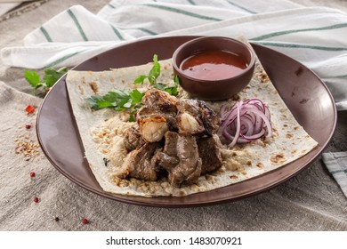 Shish kebab on lavash bread with red onion and tomato sauce on brown plate on tablecloth side view