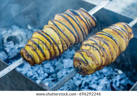 A shish kebab from yellow potatoes put on a skewer is fried on blue coals