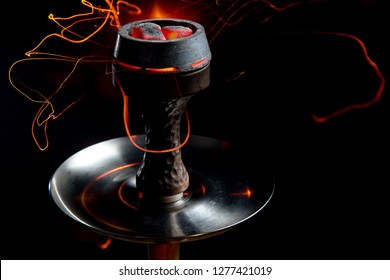 Shisha bowl with craft tobacco and red coil with hookah smoke background.