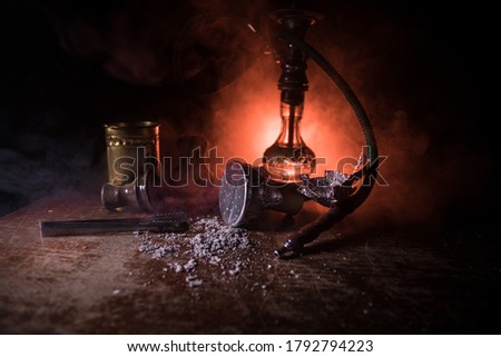Shisha concept. Preparing shisha on table. Used shisha bowl on wooden table. Dark atmosphere with light. Selective focus.