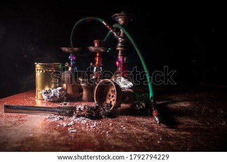 Shisha concept. Preparing shisha on table. Used shisha bowl on wooden table. Dark atmosphere with light. Selective focus.