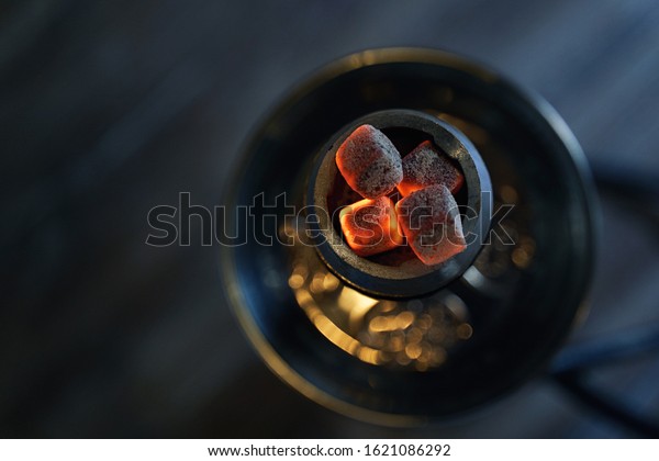 Shisha hookah\
bowl with red hot coals and craft tobacco. Modern hookah with\
coconut charcoal for relax and smoke. Beautiful sparks in long\
exposure on cozy dark lounge\
background.