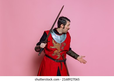 Shock. Comic Portrait Of Medieval Warrior Or Knight Wearing Wearing Armor Clothing Holding Big Sword Isolated Over Pink Background. Comparison Of Eras, History, Funny Meme Emotions