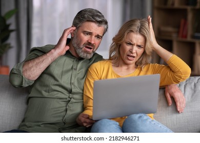 Shock Content. Frustrated Middle Aged Spouses Looking At Laptop Screen, Emotional Man And Woman Reading Bad News Online, Confused Couple Sitting On Couch At Home With Computer, Closeup Shot