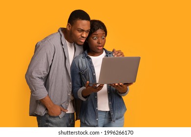 Shock Content. Overwhelmed African American Couple Looking At Laptop Screen, Young Black Man And Woman Holding Computer, Suffering From Internet Scam While Standing On Yellow Background, Free Space