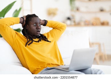 Shock Content. Shocked Young Black Man Looking At Laptop Screen And Touching Head, Confused African American Guy Emotionally Reacting To Bad News Online While Sitting On Couch At Home, Copy Space