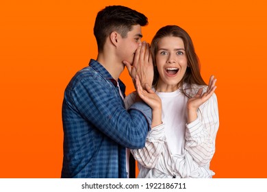 Shock, gossip, share advice and emotions of success. Young man whispering to lady on ear, happy woman with open mouth excited and surprised, isolated on orange background, studio shot, copy space