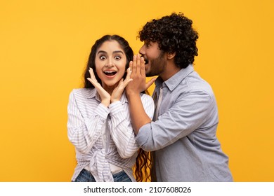 Shock, gossip, share advice. Young indian man whispering to lady on ear, happy woman with open mouth excited and surprised, posing on yellow studio background - Shutterstock ID 2107608026