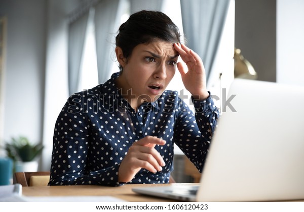 Shocked afraid worried young indian girl look at\
laptop computer screen terrified read bullying social media message\
feel bad surprise stress panic about stuck computer problem concept\
at home office