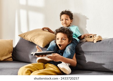 shocked african american boy holding remote control and watching movies with his cute brother - Powered by Shutterstock