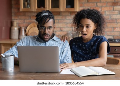 Shocked African American couple look at laptop screen frustrated by debt email paying bills online. Stunned biracial man and woman surprised by unexpected bad unpleasant news online on computer.