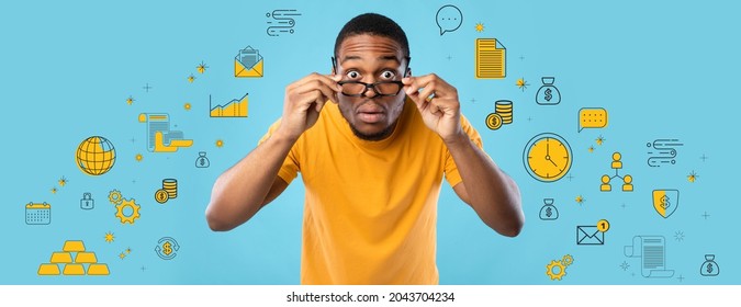 Shocked African American guy looking at camera through glasses, expressing surprise on blue studio background, collage with business, money and finance pictograms. Financial literacy concept. Panorama