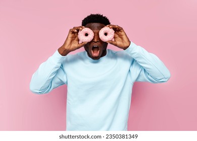 shocked african american man in blue sweater holding sweet donuts on pink isolated background, man with pastries and food screaming and being surprised - Powered by Shutterstock