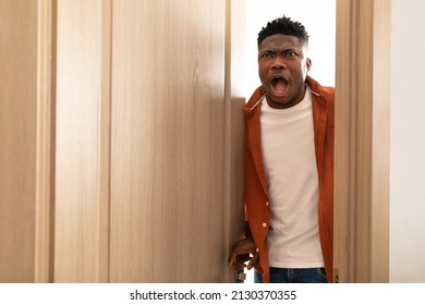 Shocked African American Man Opening The Door Looking At Something Shocking Standing With Opened Mouth At Home. Overwhelmed Guy Expressing Embarrassment. Omg, Negative News Concept