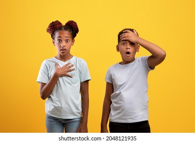 Shocked African American Teen Brother And Sister With Wide Open Eyes And Mouths Posing On Yellow Studio Background, Black Boy And Girl With Arm On Chest Siblings Looking At Something