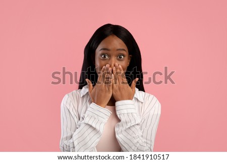 Shocked African American woman covering her mouth with hands in surprise on pink studio background. Young black lady making mistake, embarassed to hear news or gossips, cannot tell secret