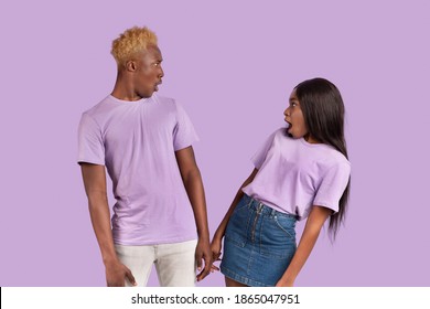 Shocked African American woman and her boyfriend looking at each other with open mouths, feeling surprised on lilac studio background. Millennial black couple screaming WOW or OMG