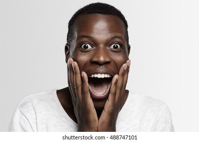 Shocked African student or employee looking at camera in full disbelief, hands on cheeks, mouth wide open, surprised with some unexpected news or big sale prices. Human face expressions and emotions