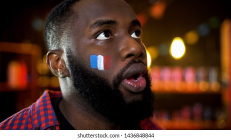 Shocked african-american man with painted french flag on cheek watching news - Powered by Shutterstock