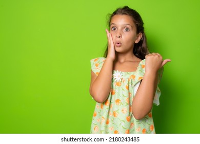 Shocked Amazed Cute Brunette Little Girl Kid, Touch Face Stunned, Turn Pointing Right Copy Space Amazed, Drop Jaw Wondered, Stare Speechless And Astonished Awesome Promo, Stand Green Background Amused