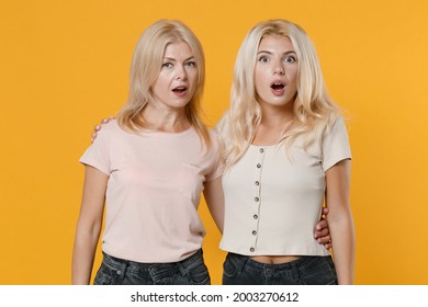 Shocked Amazed Surprised Family Two Women Blonde Mother And Daughter In Casual Clothes Standing Hugging Keeping Mouth Open Looking Camera Isolated On Bright Yellow Colour Background Studio Portrait