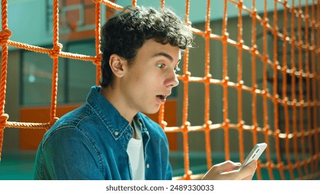 Shocked amazed wonder Caucasian teen boy student guy teenager man male son pupil in university school corridor sport hall sitting on floor shock mobile phone stunned smartphone social media addict - Powered by Shutterstock