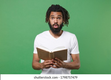 Shocked Amazed Young African American Man With Dreadlocks 20s Wearing White Casual T-shirt Posing Holding In Hands Reading Book Studying Isolated On Green Color Background Studio Portrait