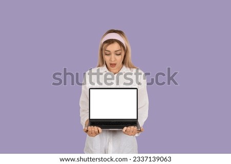 Shocked amazed young girl holding empty blank screen laptop notebook pc computer modern mock up. Looking display. Isolated pastel purple background. Technology, lifestyle, banner, advertising design.