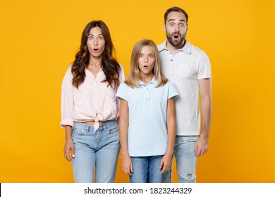 Shocked Amazed Young Parents Mom Dad With Child Kid Daughter Teen Girl In Basic T-shirts Keeping Mouth Open Isolated On Yellow Background Studio Portrait. Family Day Parenthood Childhood Concept