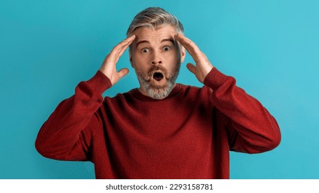 Shocked appalled middle aged grey-haired man wearing casual gesturing on blue background, touching his head and exclaiming, panorama. Human gestures and emotions concept