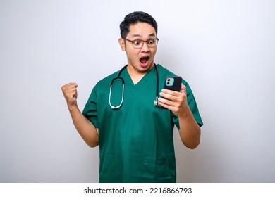 Shocked asian male doctor, nurse in scrubs and stethoscope screaming proud and celebrating victory while holding smart phone cheering emotion isolated over white background - Powered by Shutterstock