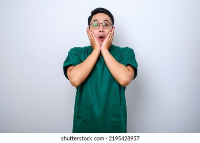 Shocked Asian Male Nurse, Doctor In Scrubs Hear Horrible News, Gasping, Cover Mouth With Hands And Stare At Camera Over White Background