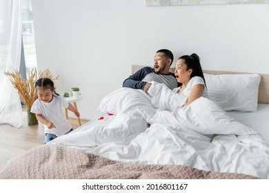 Shocked Asian Parents Looking At Toddler Daughter Running In Bedroom