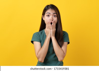 Shocked asian teenager in green tee shirt looking having shock facial emotion and open mouth on yellow background in studio.