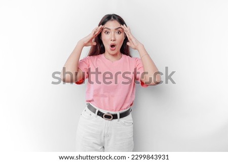 Shocked Asian woman is wearing pink t-shirt with her mouth wide open, isolated by white background