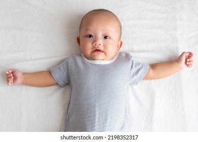 Shocked Baby Boy Wearing A Striped Shirt With A Handful Of Hands On A White Mattress