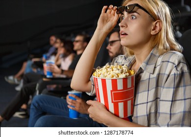 Shocked beautiful woman watching excited horror in cinema hall. Frightened attractive blonde in 3d glasses and checkered shirt keeping popcorn. Concept of entertainment and movietime.  - Shutterstock ID 1287178774