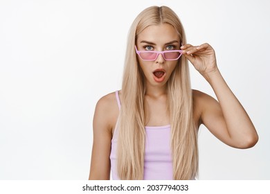 Shocked Blond Girl Takes Off Sunglasses, Say Wow And Stare Startled At Camera, Standing In Tank Top Against White Background.