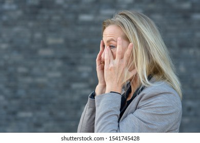 Shocked blond woman with her hands to her cheeks, looking up and screaming. Close-up side portrait against blurred grey background with copy space