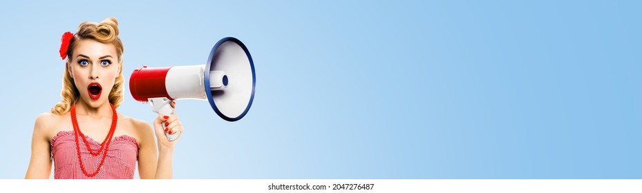 Shocked Blond Woman Holding Mega Phone And Shout Something. Girl In Red Pin Up Style With Wide Open Mouth, Light Blue Background With Copy Space. Female Model In Retro Vintage Studio Concept. Sales Ad