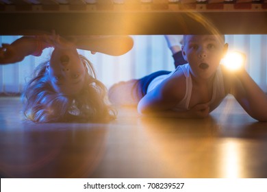 The Shocked Boy And Girl With A Flashlight Look Under Bed. Night Time