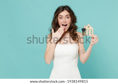 Shocked bride young woman 20s in white wedding dress hold house bunch of apartment keys cover mouth with hand isolated on blue turquoise background studio portrait. Ceremony celebration party concept