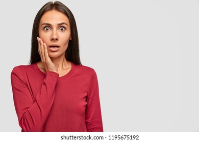 Shocked brunette woman looks with bated breath at camera, cant believe in failure, has eyes popped out, dressed in casual red sweater, isolated over white background with copy space for your promotion - Shutterstock ID 1195675192