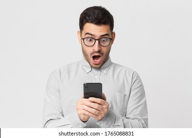 Shocked Business Man In Casual Shirt Looking At His Phone With Surprise Expression, Isolated On Gray Background 