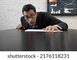 Shocked businessman with bugged eyes after bad news about his business sitting at the desk with documents. Crisis at work and stress concept