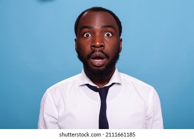 Shocked businessman looking surprised with open mouth facing unbelievable situation on blue background. Amazed person with big eyes jaw dropping. Astonished office worker.