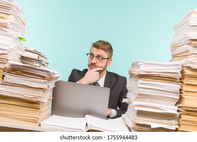 Shocked businessman sitting at the table with many papers in office, he is overloaded with work - image