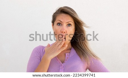 Shocked Caucasian woman covering mouth with hand. Portrait of surprised mature female model with fair hair in lilac blouse looking at camera, reacting to news. Shock, gossip concept