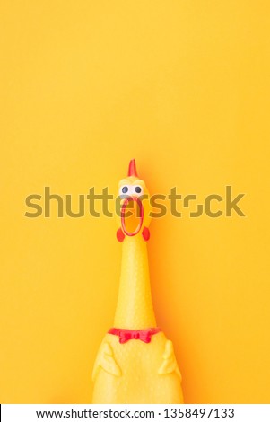Shocked chicken toy is isolated on a yellow background, looks into the camera and yells. Toy chicken, shouting with a mouth open on a yellow background. Isolated